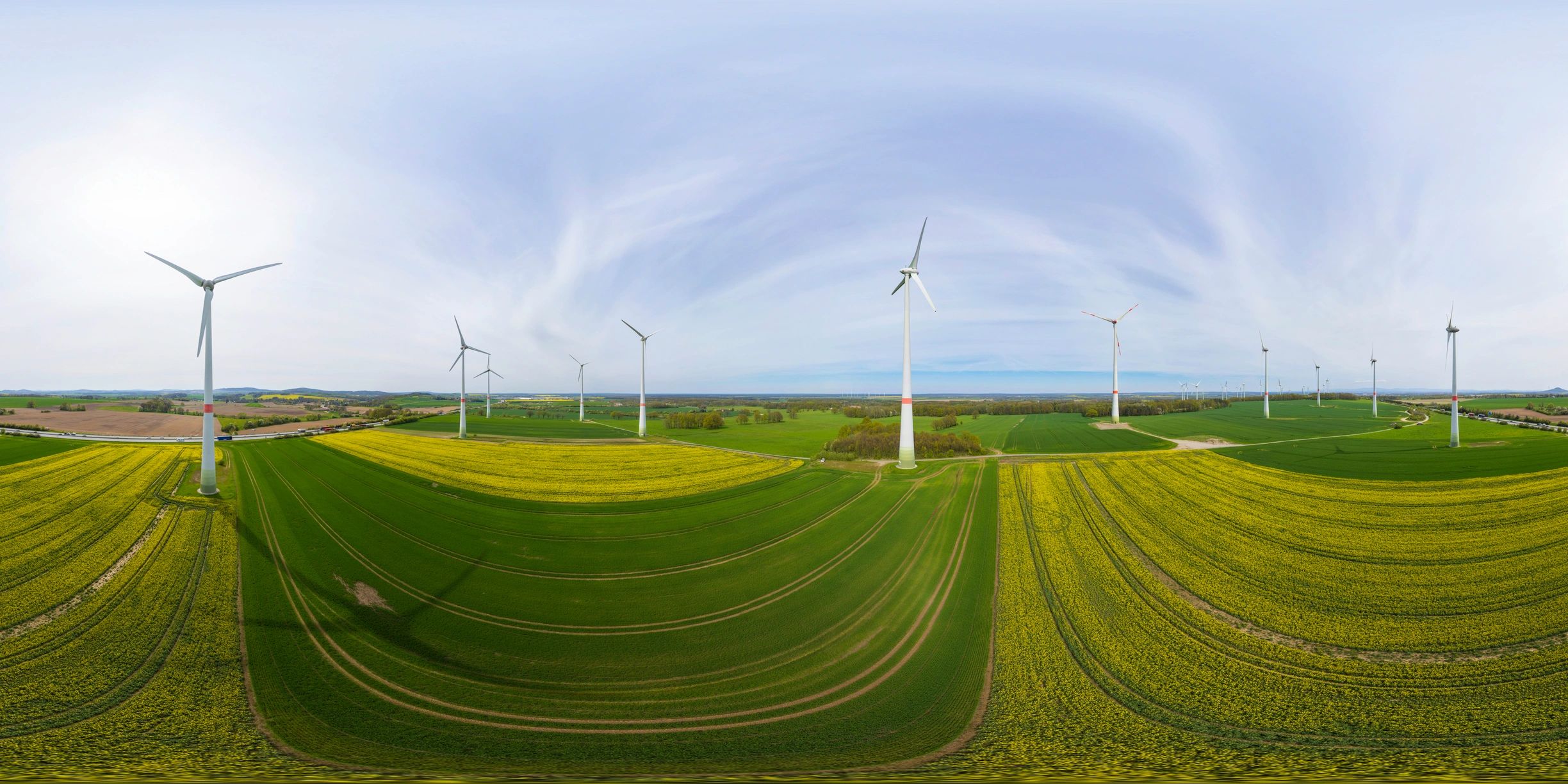 Panoramic view of wind turbines across green fields under a bright blue sky